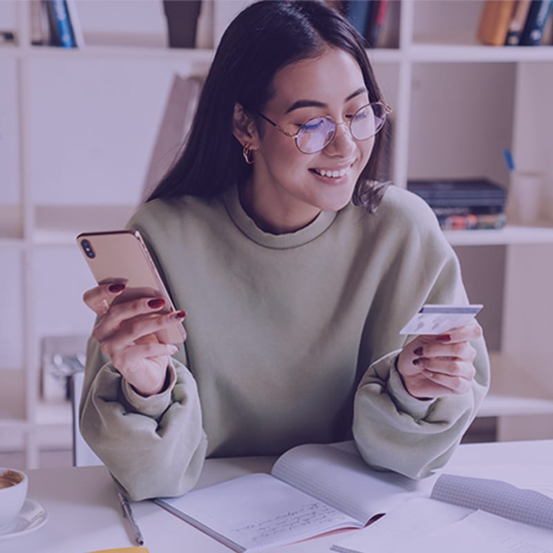 A young, smiling female holding credit to make an online payment via smartphone