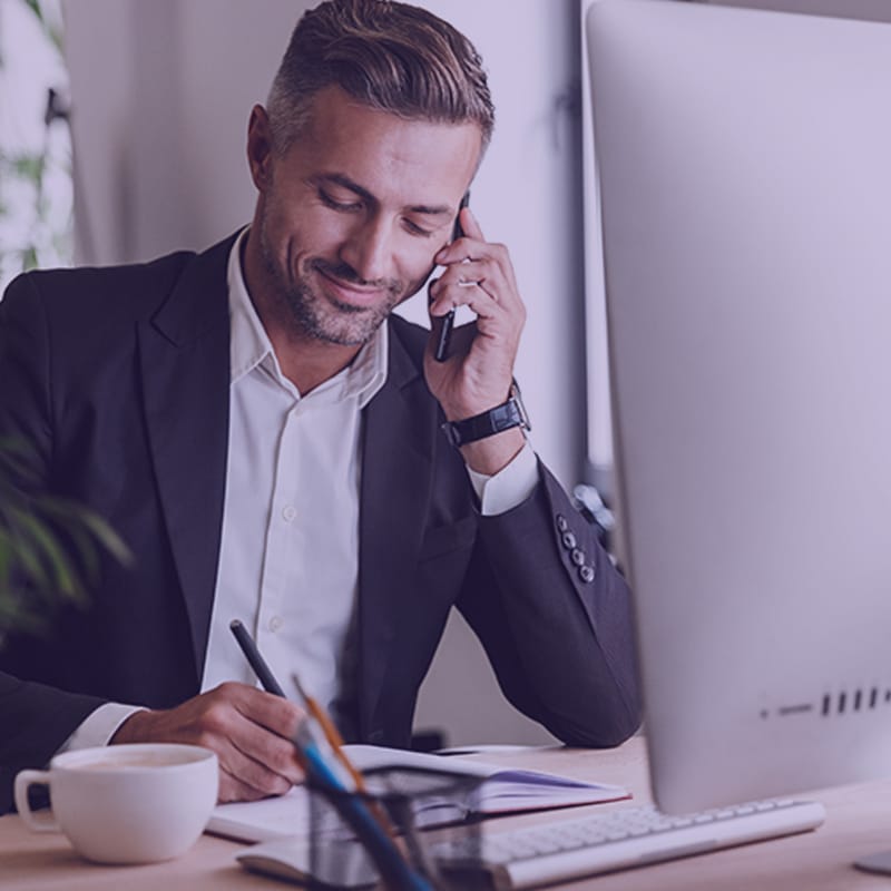 Businessman talking on cell phone while working on computer in office